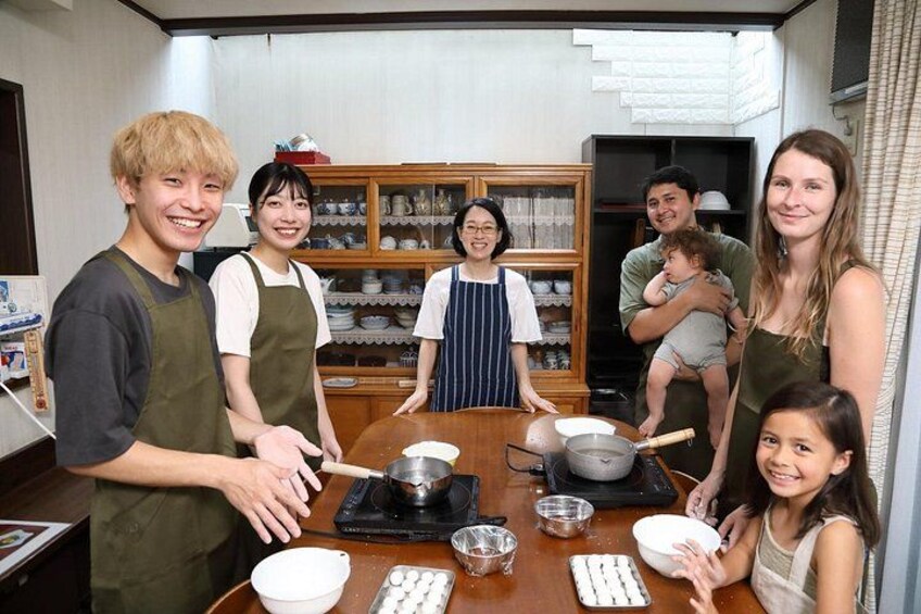 A family cooking together in a kitchen with a wooden table, pots, and bowls. 1