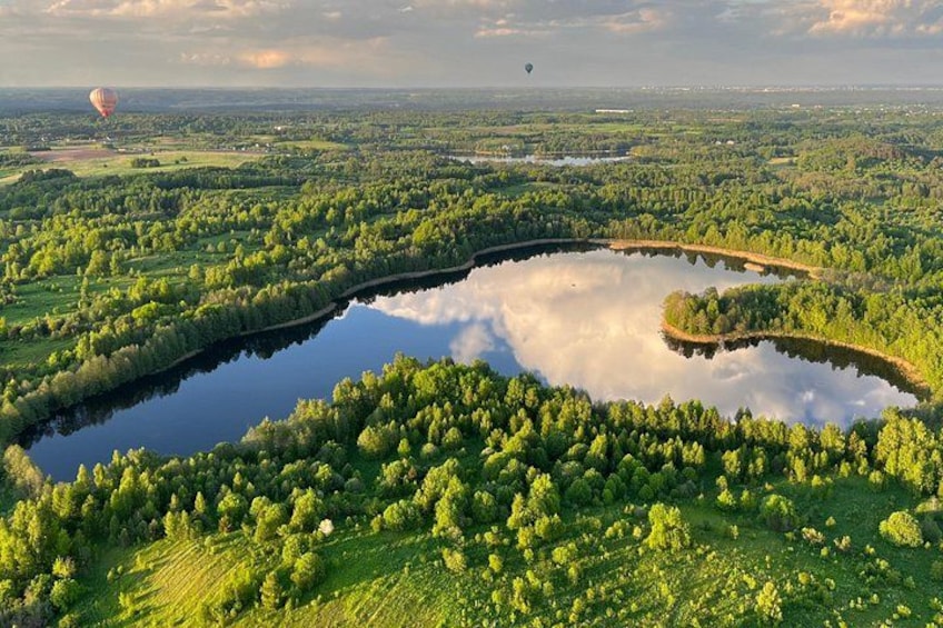 A lake surrounded by dense forest, a hot air balloon in the distance, and a clear sky. 2