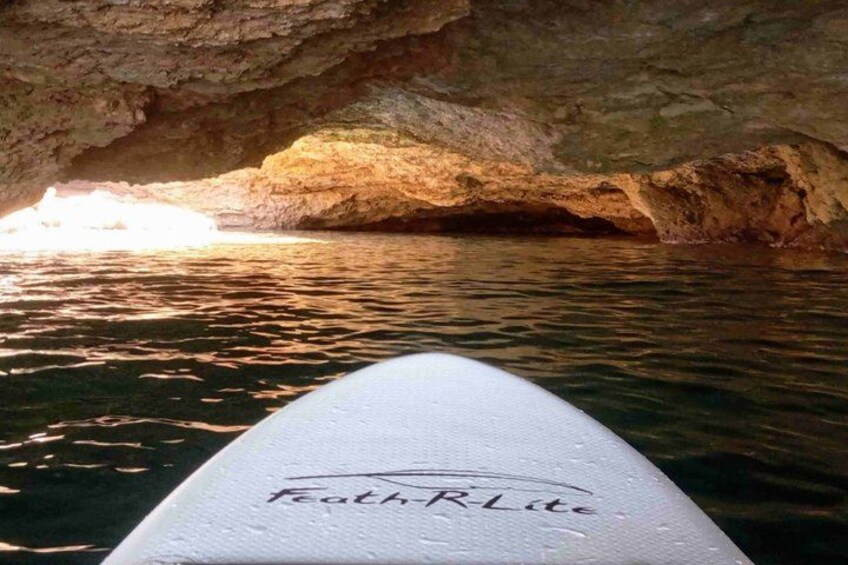 Une planche de surf sur laquelle est inscrit « Feath’r Lite », l’entrée d’une grotte et une eau calme. 5
