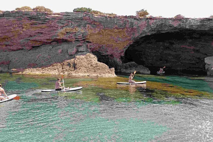 Kajakkers op een rustig wateroppervlak met helder turquoise water, omringd door rotsachtige kliffen met paars en groen groen.' 2