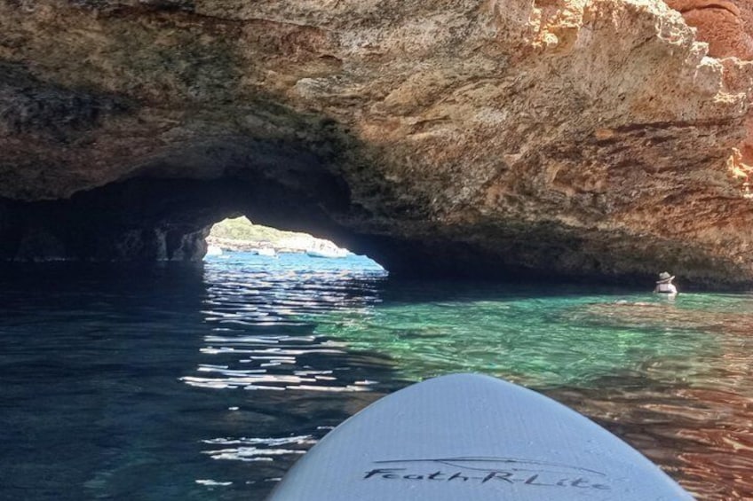 A rocky cave opening to clear blue water, a surfboard, and a person swimming. 2
