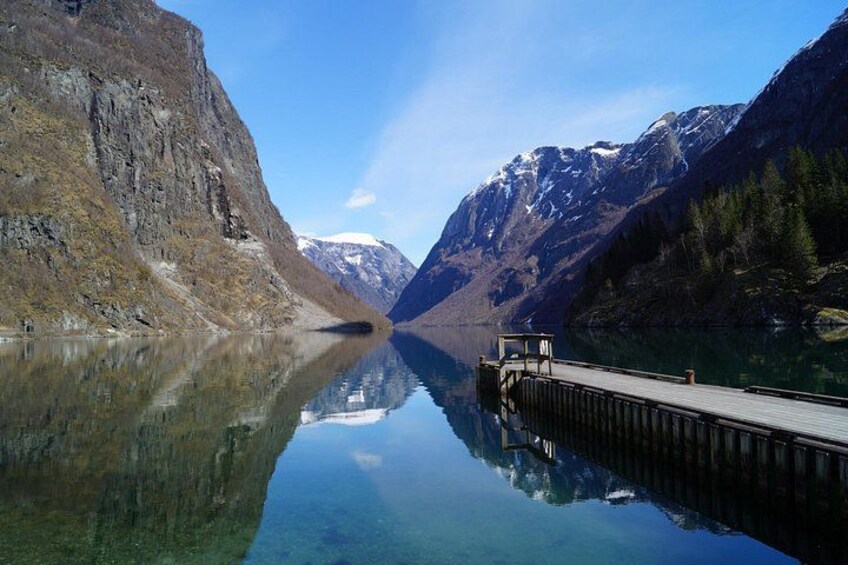 A calm lake with a wooden dock extending into the water, surrounded by mountains and clear skies. 2
