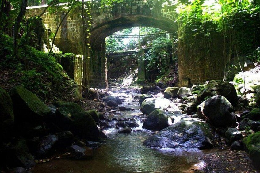 A stone bridge over a stream with rocks and greenery. 1