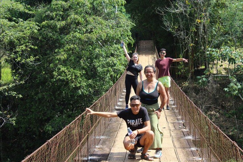A group of people on a wooden suspension bridge surrounded by dense greenery. 1
