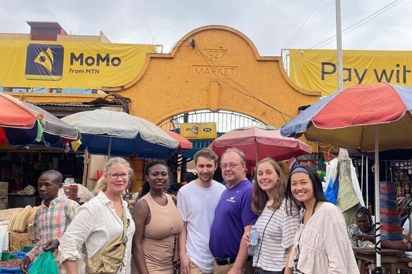A group of people standing in front of a market with umbrellas and a yellow sign. 3