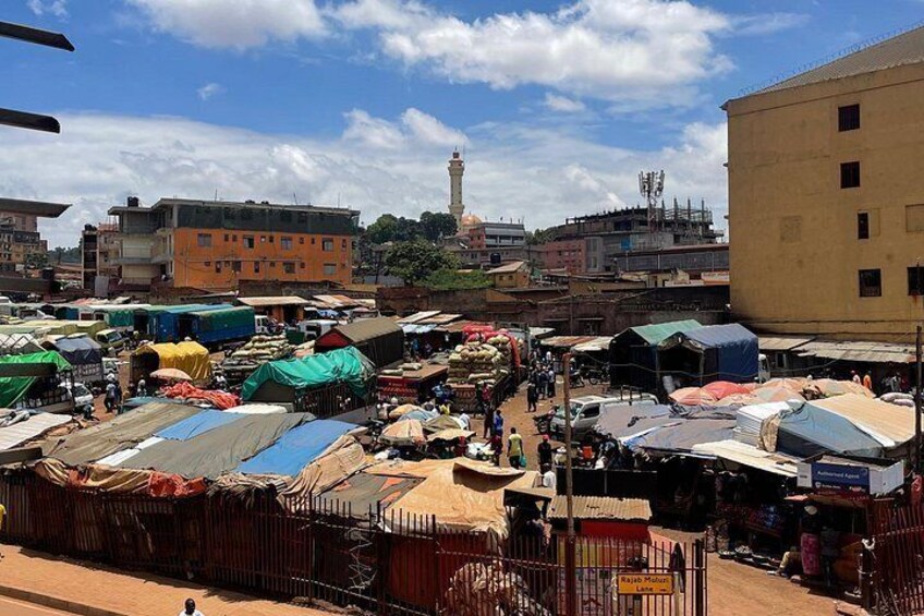 A bustling outdoor market with various stalls and tents, surrounded by buildings and a prominent tower in the background. 4
