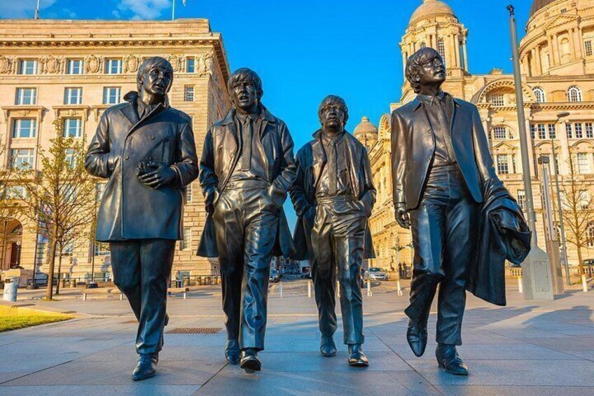 A statue of four men in suits walking on a sidewalk. 4