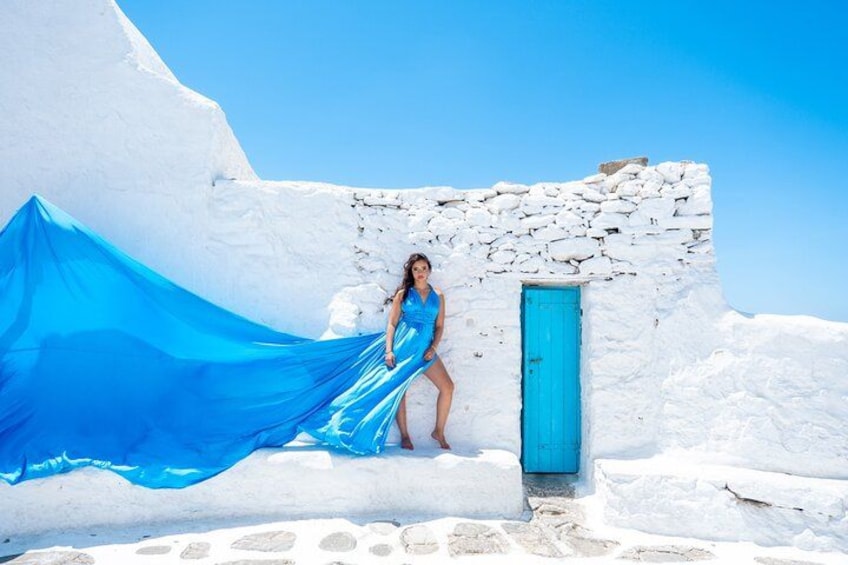 Una persona con vestido azul de pie frente a un edificio blanco con puerta azul. 5