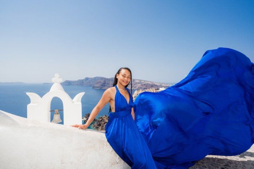 Una persona con un vestido azul de pie cerca de una iglesia blanca con vista al mar. 3