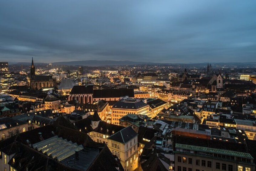 A cityscape at dusk with illuminated buildings and a prominent church spire. 2