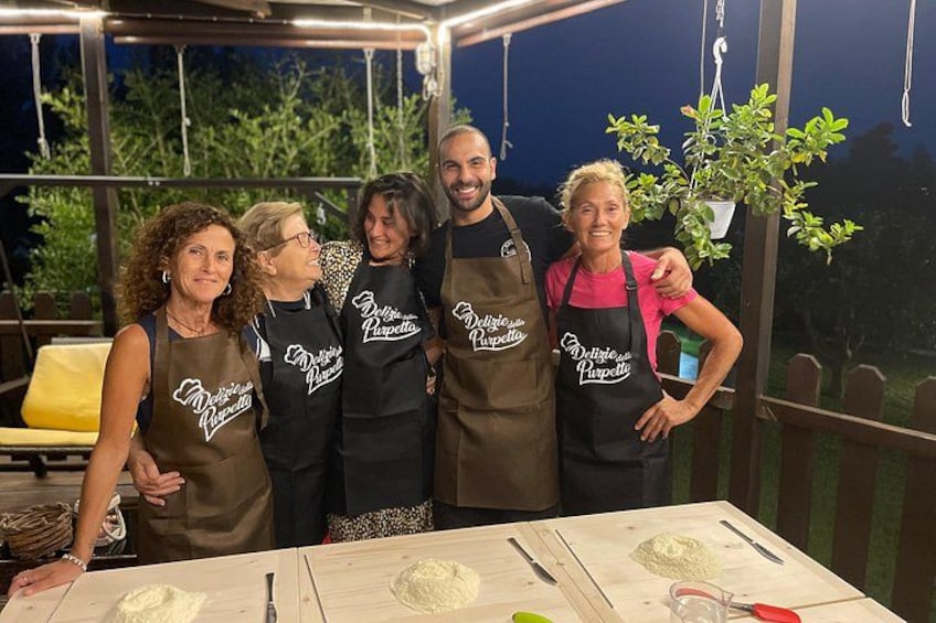 A group of people wearing aprons with 'Delizie di Puzza' on them, standing around a table with food items. 3