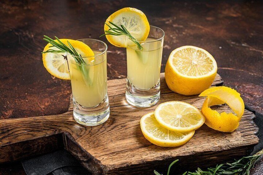 Two glasses of a lemon-based drink with lemon slices and rosemary on a wooden board. 2