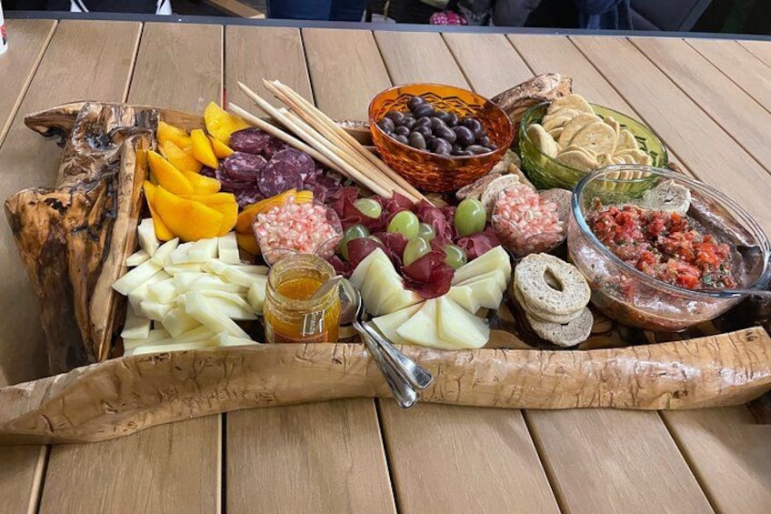 A wooden table with a charcuterie board featuring various cheeses, fruits, olives, and crackers. 4