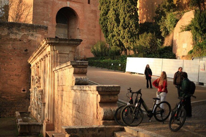 Un arco de piedra, una bicicleta y personas caminando en un parque. 2