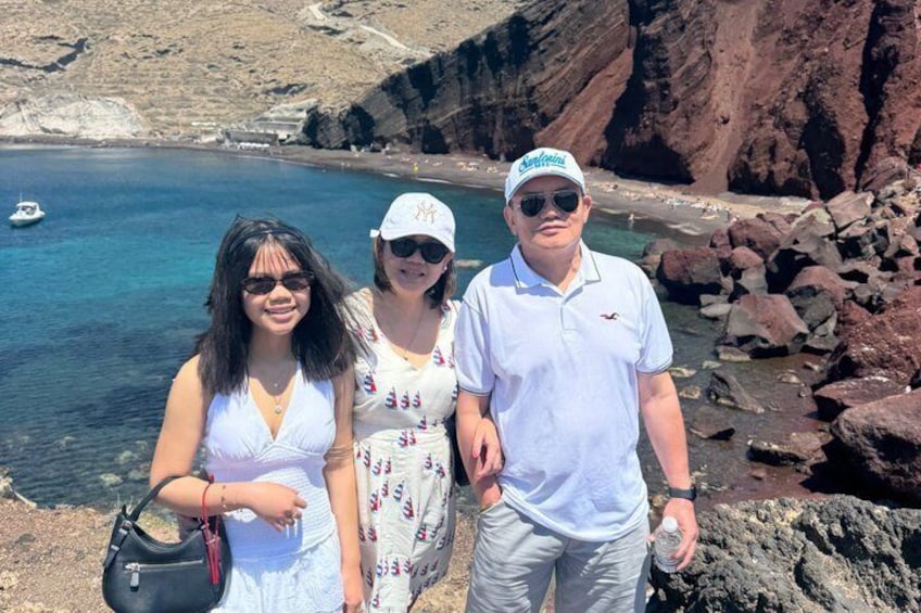 Three people standing on a rocky beach with clear blue water and a boat in the distance. 3