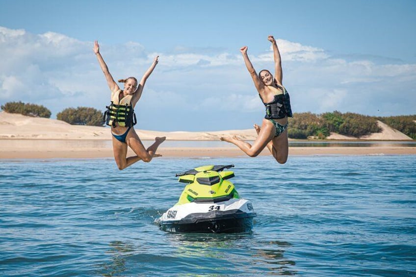 Two people jumping off a jet ski into the water. 1