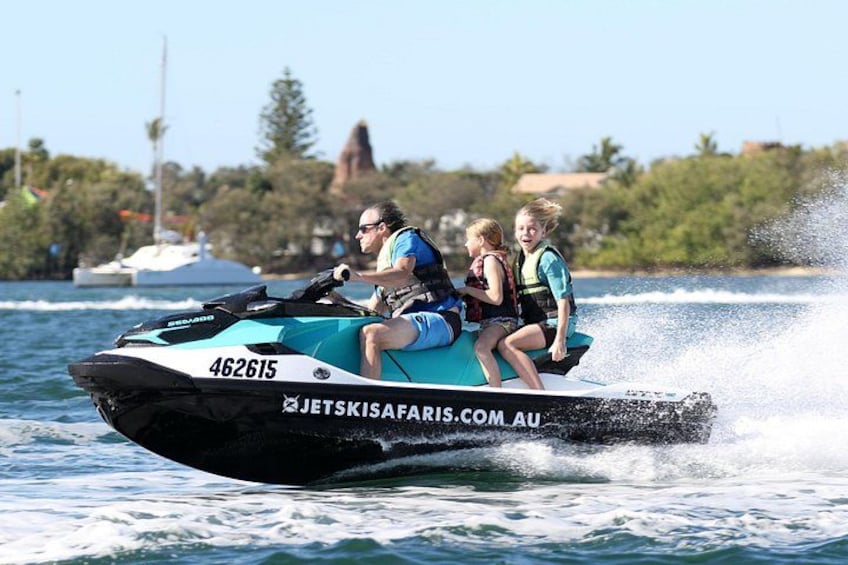 A jet ski with three people on it, water splashing around, and a clear sky in the background. 2