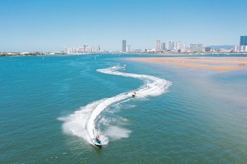 A jet ski creating a wake in turquoise water with a city skyline in the background. 3