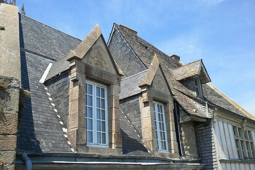 A stone building with a steeply pitched roof, a central window, and a decorative crest. 3