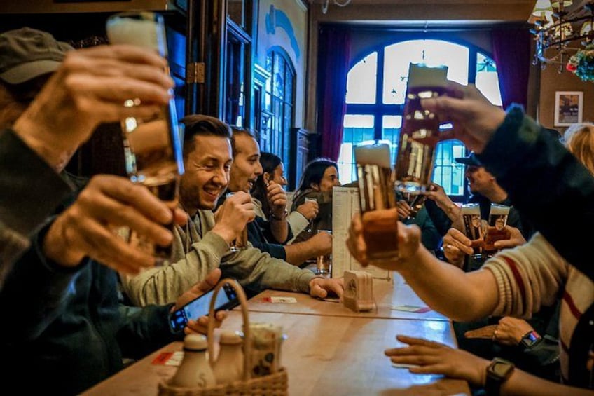 A group of people toasting with drinks at a table in a restaurant with arched windows and a chandelier. 1