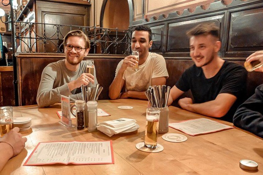 Three people sitting at a wooden table in a restaurant, with menus, glasses of beer, and condiments. 3