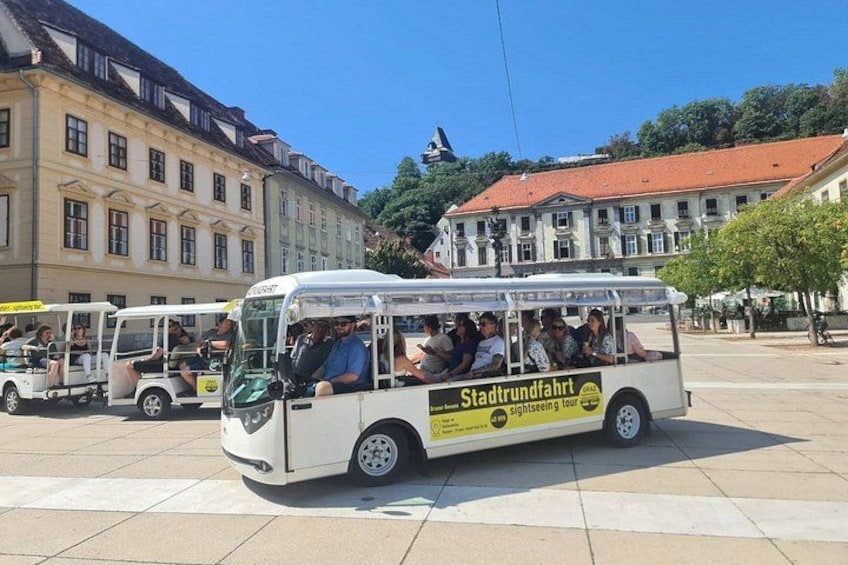 A city tour bus with passengers, surrounded by historic buildings and a clear sky. 4