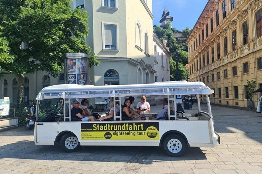 A white tour bus with passengers, parked on a cobblestone street, surrounded by historic buildings. 2