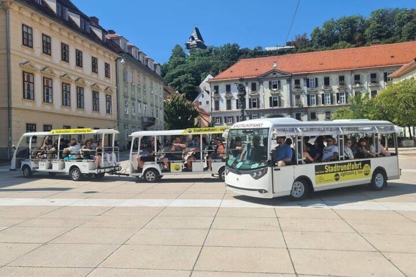 Una plaza de ciudad con tres autobuses blancos identificados con el nombre 'Stadtverkehr' y turistas. 1