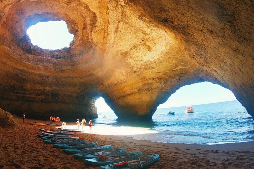 Una cueva que desemboca en el mar, con kayaks alineados en la playa y gente cerca del agua. 4