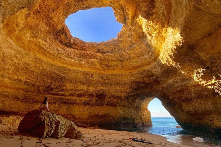 Una persona sentada sobre una roca dentro de una cueva grande, con vista al océano. 1