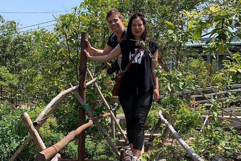 Two people climbing a bamboo structure in a garden with trees and a traditional building in the background. 4