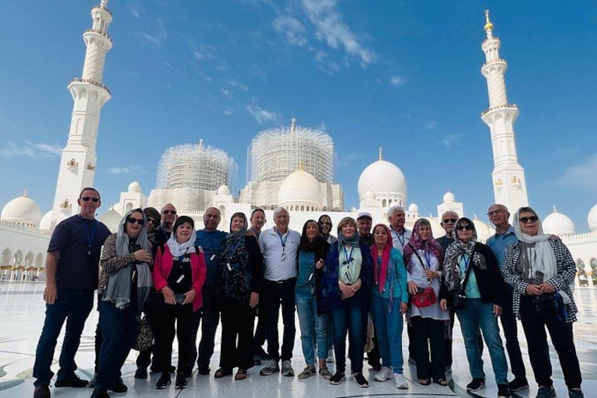 Een groep mensen staat voor een witte moskee met meerdere koepels en minaretten. 4