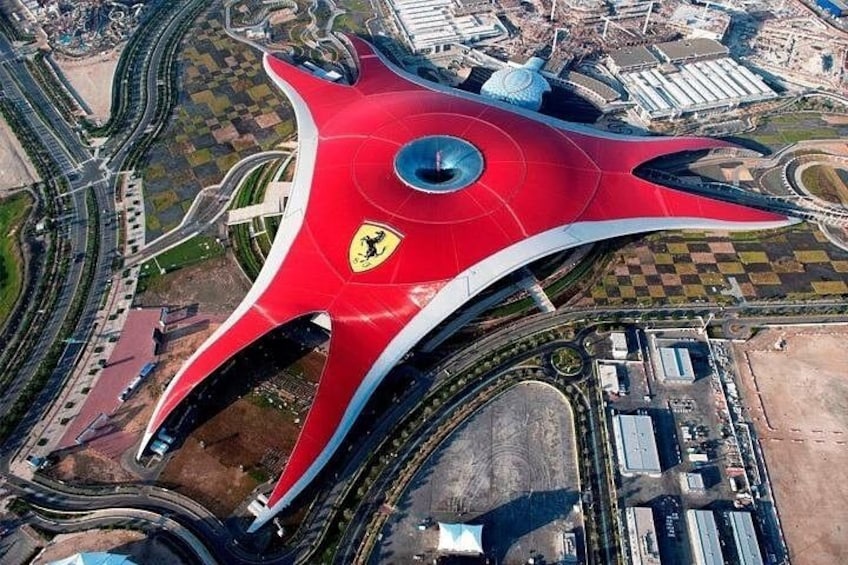 Een rode, futuristische constructie met een Ferrari logo, omringd door wegen en gebouwen. 1
