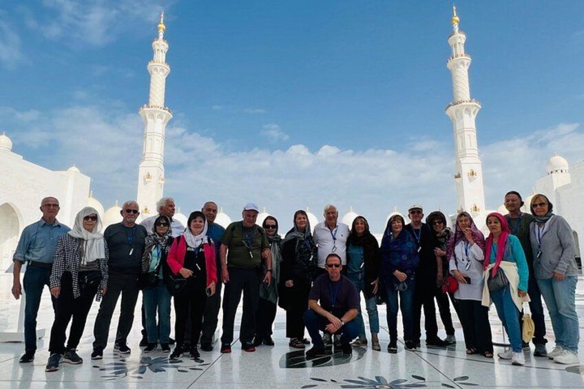 Een groep mensen staat voor witte minaretten, met een heldere lucht. 5