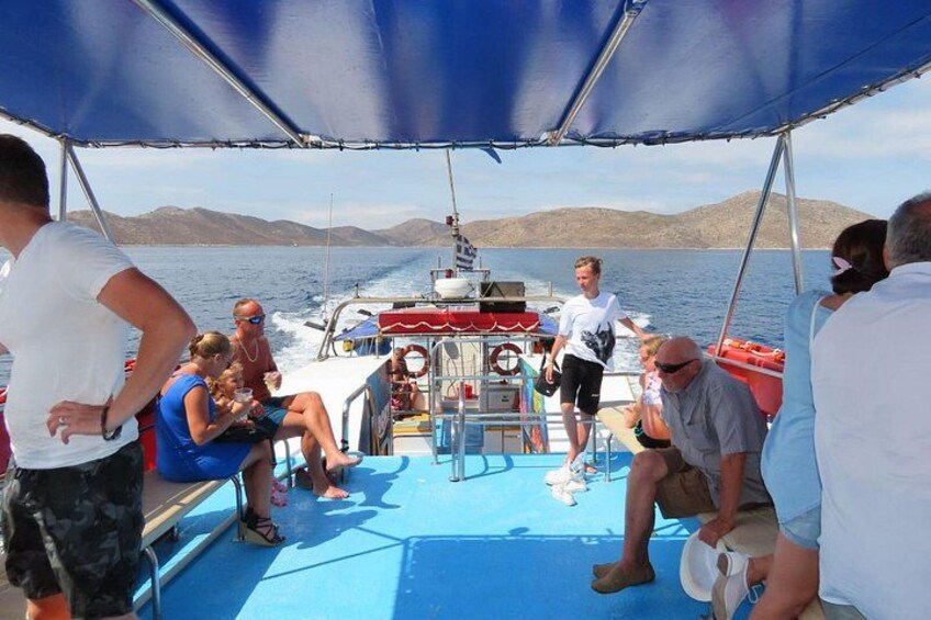 Eine Gruppe von Menschen auf einem Boot mit einem blauen Deck, einem Vordach über ihnen und einer bergigen Landschaft im Hintergrund. 4