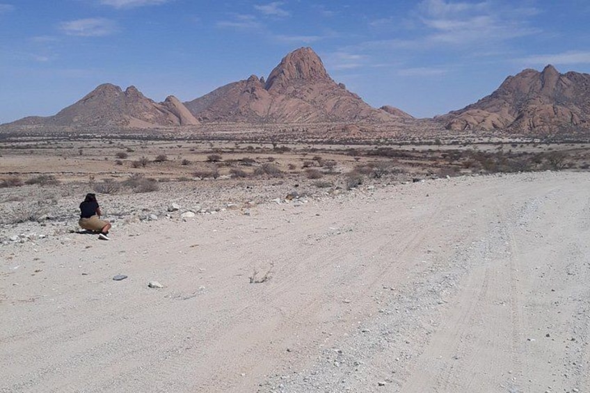 Un paysage désertique avec une personne assise par terre, des montagnes en arrière-plan et un ciel dégagé. 5