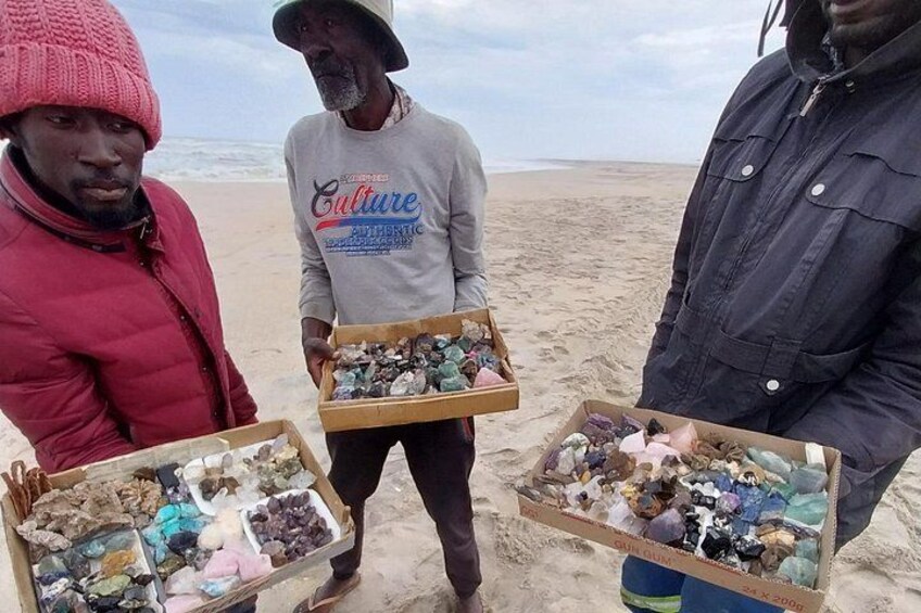 Trois personnes se tiennent sur une plage, chacune tenant une boîte contenant différents minéraux. 4