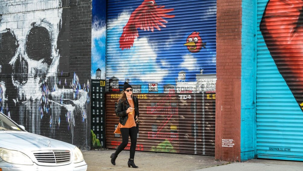 Une femme passe devant une fresque murale et les volets fermés d’un magasin. 1