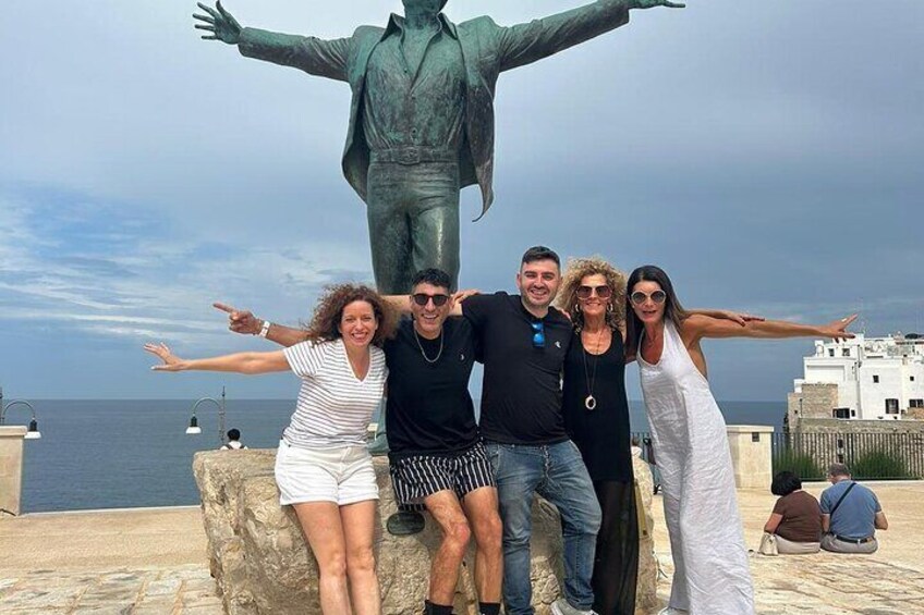 A group of people posing in front of a statue with outstretched arms, a body of water, and buildings in the background. 5