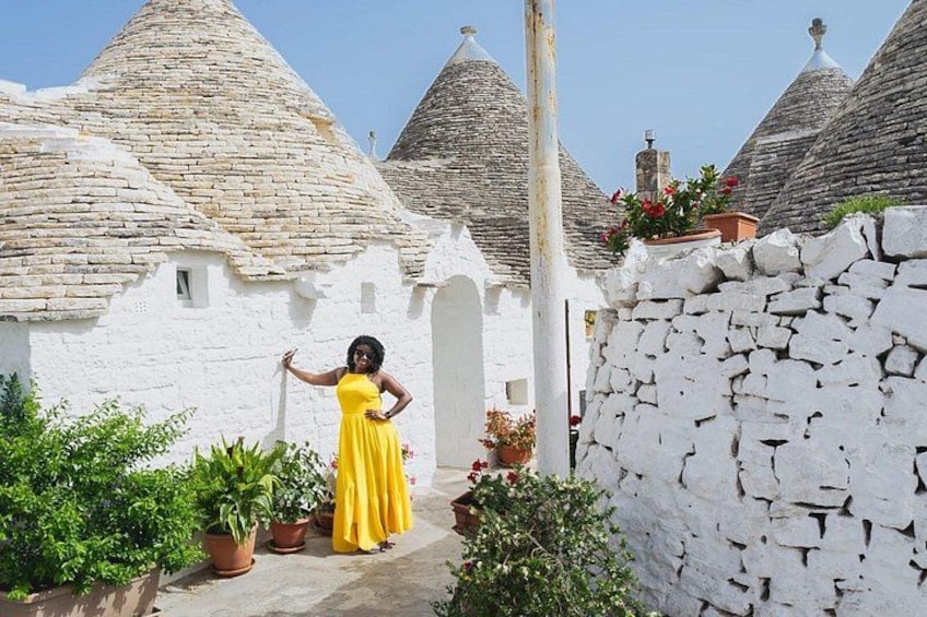 A woman in a yellow dress standing in front of traditional stone houses with conical roofs. 5