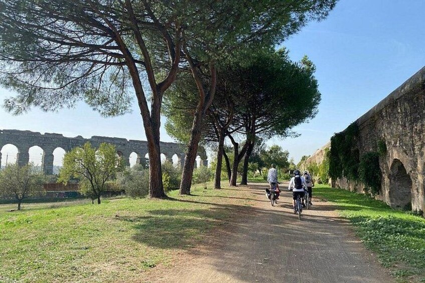Un chemin pavé, avec des cyclistes, des arbres et, au loin, un ancien pont de pierre. 2