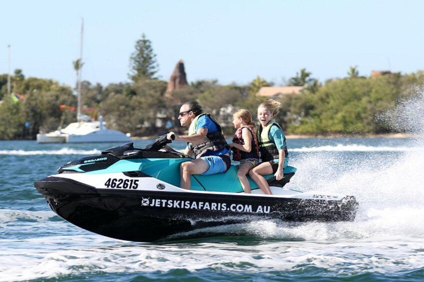 Un jet ski con tres personas, salpicaduras de agua y un cielo despejado al fondo. 3