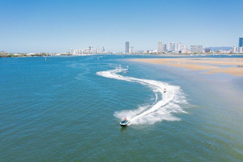 A jet ski creating a wake in calm blue waters with a city skyline in the background. 1