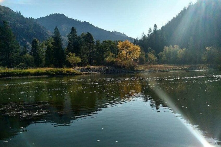 A calm river with reflections, surrounded by trees and mountains. 5