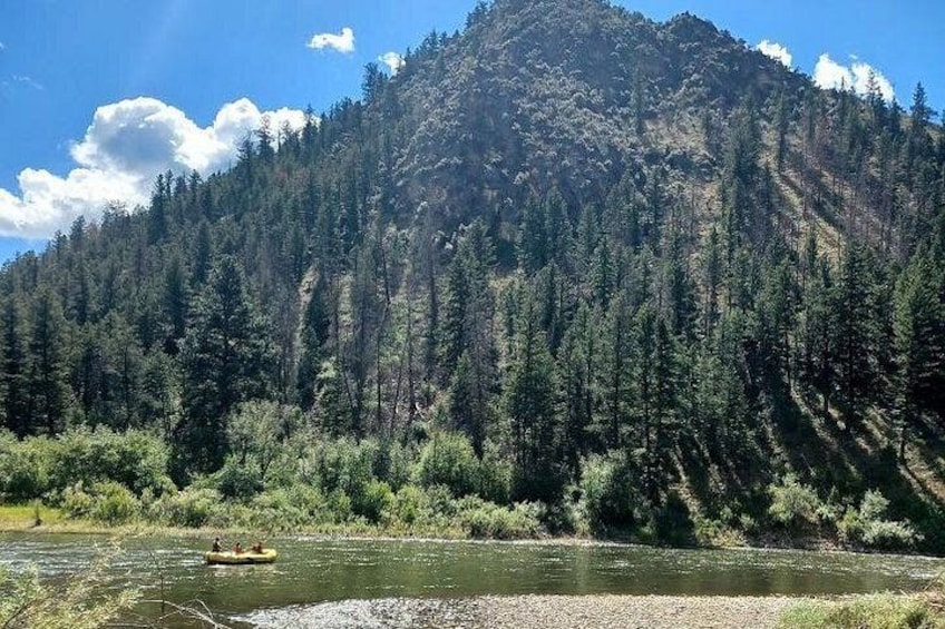 A river with a raft, surrounded by dense forest and a mountain. 1