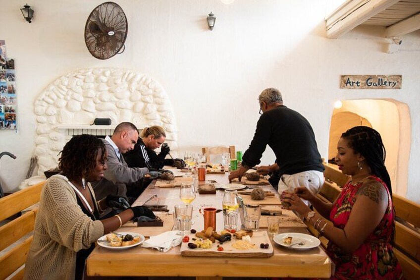 Eine Gruppe von Personen speist an einem Holztisch in einem Restaurant, an der Wand ist ein Schild für eine Kunstgalerie zu sehen. 2