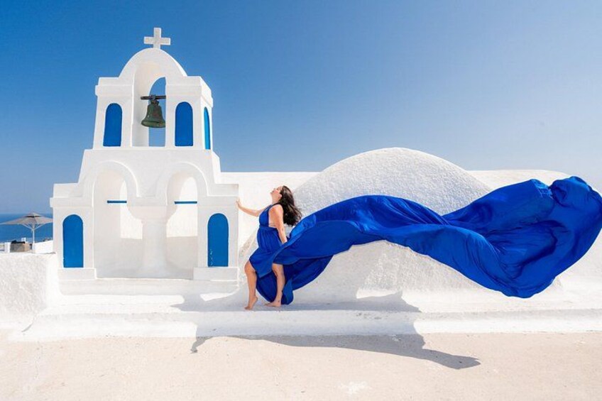 Eine Person in einem blauen Kleid in der Nähe einer weißen Kirche mit einem Glockenturm, vor blauem Himmel. 1
