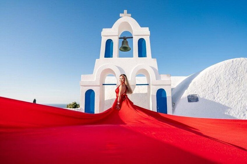 Una donna con un abito rosso in piedi di fronte a una chiesa bianca con porte blu e un campanile. 3