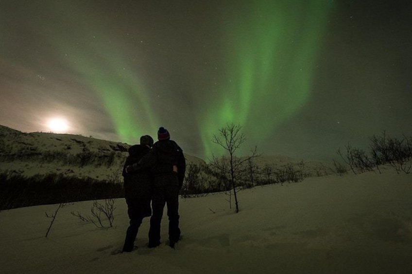 Dos personas de pie en un paisaje nevado, con la aurora boreal de fondo. 5
