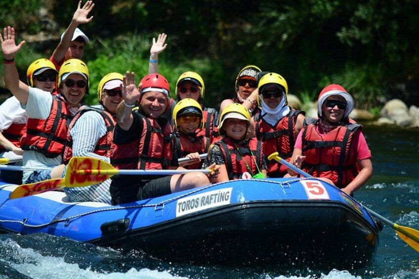 Un grupo de personas en una balsa azul con el número 5, usando chalecos salvavidas y cascos, en un río. 3